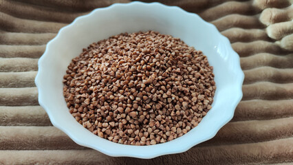 A white plate with brown buckwheat. Brown buckwheat groats for background and texture. Partial focus