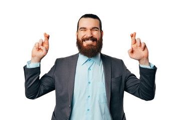 Bearded man wearing jacket with eyes closed and fingers crossed makes a wish.