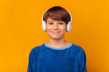 Young smiling at camera teen boy is wearing headphones and enjoying music.