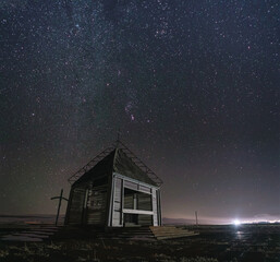 small wooden church in a field under a starry sky