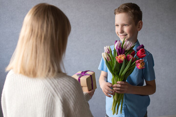 Fototapeta na wymiar Cute boy gives a bouquet of tulips and a box with a gift to mom