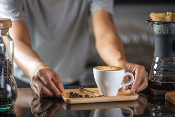 White ceramic cups of cappuccino with latte art Barista make coffee by pouring spills hot milk cream on black coffee. Barista serve holding cup of hot latte and coffee beans on wooden table cafe shop