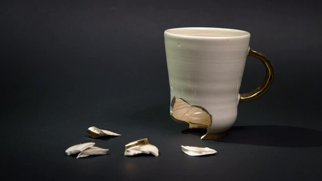 Broken tea cup isolated on black background. Cracked coffee mug and fragile ceramic pieces