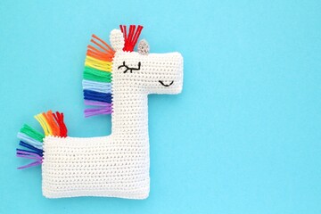 Crochet amigurumi handmade stuffed soft white unicorn toy with rainbow mane on blue background....