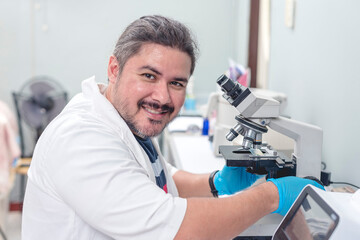 A cheerful male laboratory technician making a thumbs up while checking a swab sample with a...