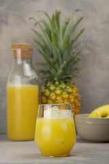 Pineapple juice in a clear glass and bottle on a light table. Pineapple and slices in the background.