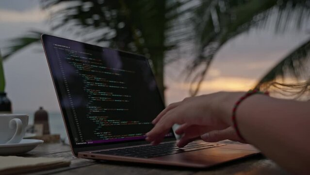 Female developer working on laptop by the ocean. Young woman freelancer coding at outdoor tropical cafe. Caucasian girl working remotely typing on computer at exotic location close-up. Worldwide work.