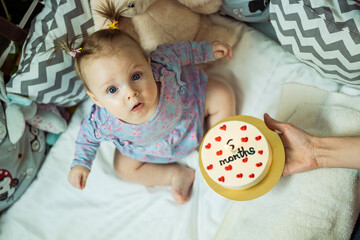 Cute baby girl celebrates 6th month from the birth. Happy little girl gets cake with candle. Daughter 6th month party.