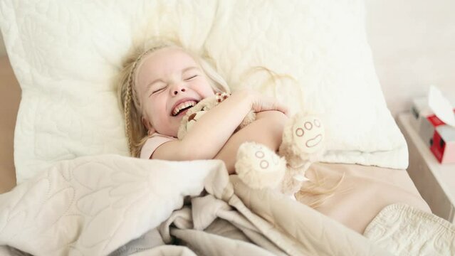 Portrait of happy sleepy little girl kid hug bear waking up lying in bed at light room Pretty child laughing enjoying early awaking before school in cozy bedroom Beautiful morning and good day concept