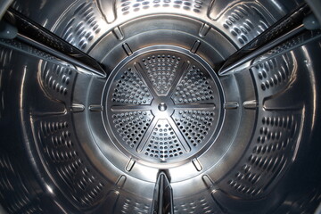 Washing machine or tumble drier metal perforated empty drum. Inside wide-angle view, no people