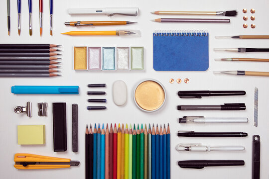 Designer work tools flat lay composition on white background. Painting, sketching, drawing activity, prepared work space. Objects as watercolors, paint brush, pencil, marker, pen and more supply.