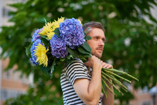 man smiling holding a bouquet of hydrangea and yellow flowers looking aside on the background of green garden. High quality photo