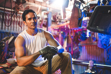 Fototapeta na wymiar Young and handsome muscular and strop scrap material man in sleeveless shirt sitting on material in junkyard while looking away while taking rest and break from work during in warehouse