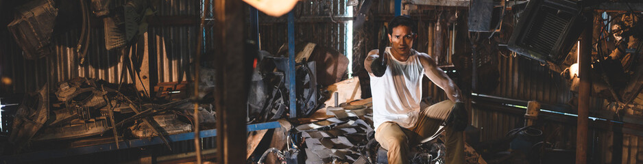 Young and handsome muscular and strop scrap material man in sleeveless shirt sitting on material in...