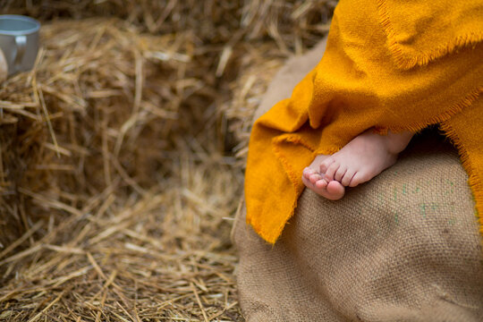 Bare feet of a little girl wrapped in turmeric-colored linen on burlap against a background of straw
