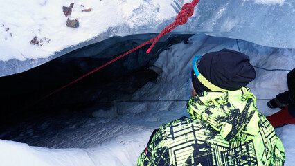 A climber descends by a safety rope into an ice cave in a glacier. The gray-blue color of ice....