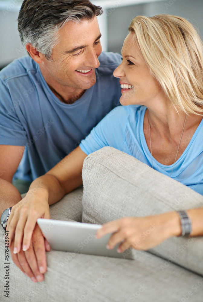 Poster sharing a little laugh online. a smiling couple sitting at home using a digital tablet.