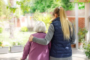 Professional young helpful caregiver walking with the elderly woman in the garden at nursing home. Elderly care concept