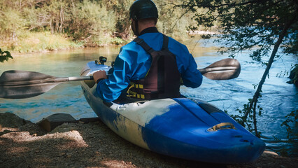 Male kayaker sitting in a kayak and holding the paddle, pushing away from the high bank and...
