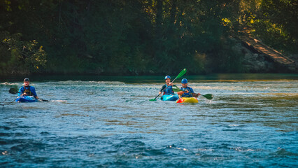 Three kayakers paddling and maneuvering on the fast-moving river with a rocky shore and going under the concrete bridge