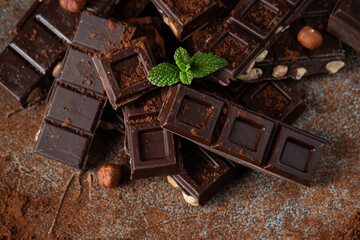 Dark and milk chocolate with nuts on a dark background sprinkled with cocoa powder.