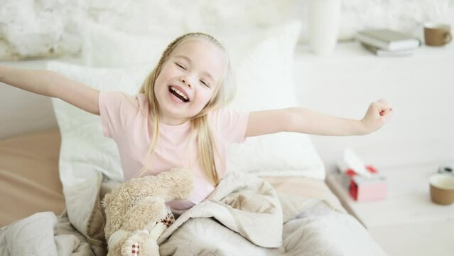 Portrait of happy sleepy little girl kid waking up lying in bed at light room Pretty child stretching enjoying early good morning before school in cozy bedroom Beautiful morning and good day concept