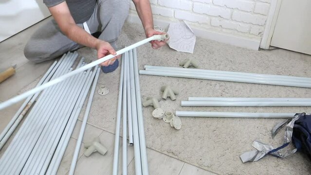 A man checks the assembly of the knots of a garden tent. Parts for assembly are laid out on the floor.