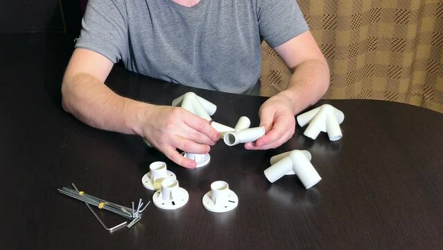 A man demonstrates a set of parts for a garden awning. Examines adapters and supports. Medium plan.