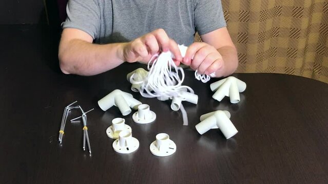 A man demonstrates a set of parts for a garden awning. Examines twine and pegs. Medium plan.