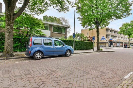 Amsterdam, Netherlands - 10 April, 2021: a small blue car parked on the side of the road in front of a building with trees lining the street