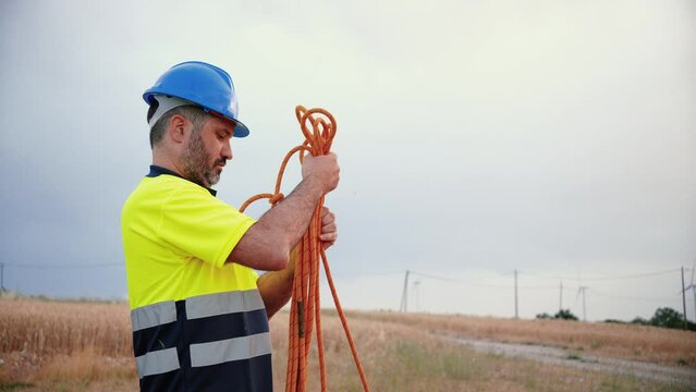 Construction worker or contractor, rolling up rope wearing a blue hardhat and security vest. Workman picking up his tools. Industry concept. Slow motion. High quality 4k footage
