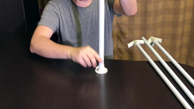 A man demonstrates parts for a garden awning. Connects tubes and adapters. Medium plan.