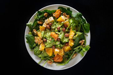 Zenith view of spinach and lettuce salad and orange with hazelnuts, sesame and romesco sauce, white...