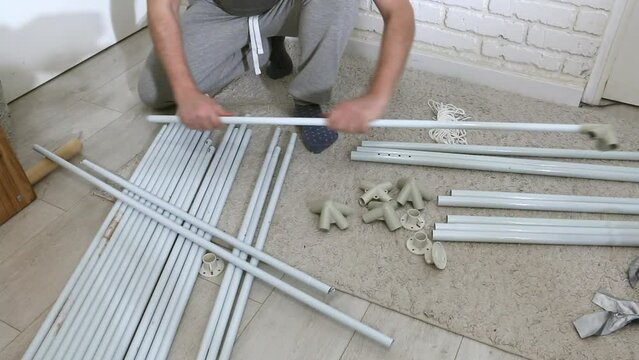 A man is putting together a garden tent. Connects tubes and adapters. Parts for assembly are laid out on the floor.