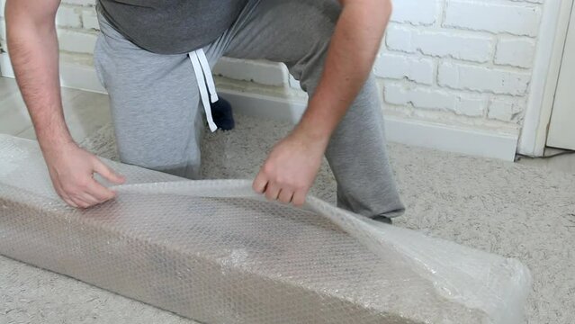 A man unpacks a package. Rip off the packing tape. Garden tent in bubble wrap