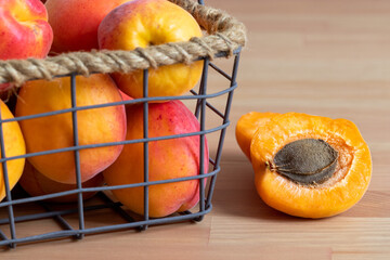 Sliced and whole apricots in a minimal basket placed on a wooden table. Pile of a fresh bio apricots with one piece cut in half.