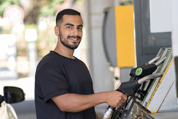 Fototapeta na wymiar Handsome middle eastern man looking camera and preparing refueling his car at the gas station. Happy guy smiling in filling station in city 