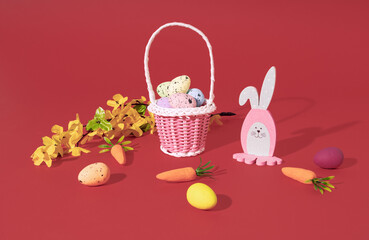 Easter Bunny, eggs in basket, carrots and spring tree branch on red background. Minimal horizontal composition, Easter decoration concept