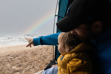 Dad and son in a tent by the sea . Dad shows a bright rainbow to the baby was given . The concept of alternative parenting, travel and vacations with family.