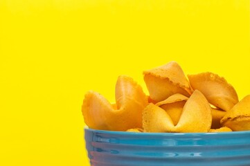 Unopened fortune cookies in a blue ceramic bowl partial, isolated on a yellow background with copy space.