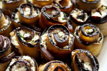 Eggplant rolls parmesan. Appetizer stuffed eggplant. Grilled eggplant roll with feta cheese in a plate on a wooden kitchen table. Closeup. Copy space. Out of focus