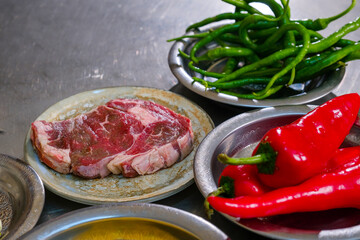Meat dish preparation in restaurant kitchen. Raw meat on plate and blurred behind paprika, green pepper