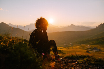 Berg-Panorama in den Alpen bei Sonnenuntergang im Sommer mit Silhouette einer sitzenden Frau - obrazy, fototapety, plakaty