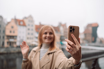 Selfie time. Young happy lady in a spring vacation, walking in the city photographing herself on a foggy day. Gdansk Poland Europe