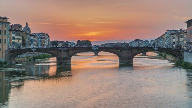 Cityscape viewfrom above on Arno river with famous Holy Trinity bridge timelapse on the sunset in Florence. Reflections on water. Orange sky