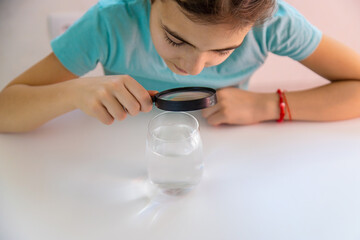 The child examines the water under a magnifying glass. Selective focus.