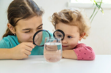 The child examines the water under a magnifying glass. Selective focus.