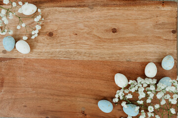 Dyed eggs and white small flowers lie on wooden brown table. Space for text. Mock up. Wooden background with blue and white eggs and white flowers for easter. 