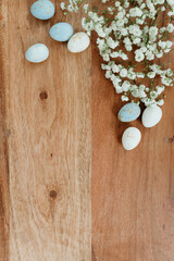 Dyed eggs and white small flowers lie on wooden brown table. Space for text. Mock up. Wooden background with blue and white eggs and white flowers for easter. 