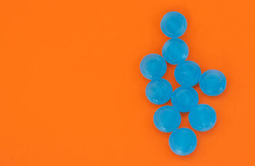 blue lozenges on orange surface,stethoscope on rock heap stack of plastic blister packs one over another,surgical gloves.hand remove from blister one candy.ear tips tubes in shadow sun.medical tablets
